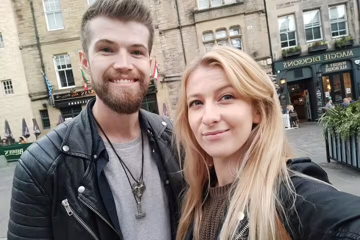 Couple smiling on Edinburgh's historic Royal Mile street with stone buildings in background