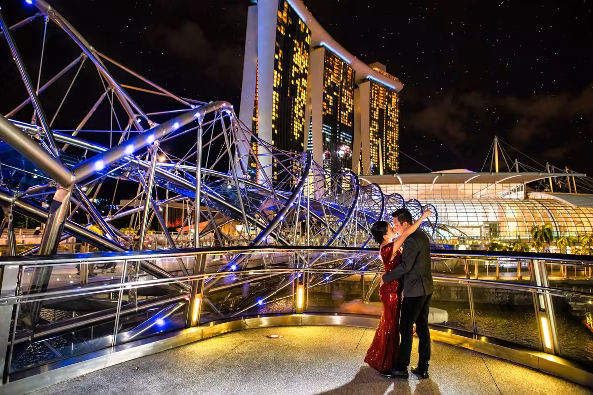 Couple embracing on Helix Bridge in Singapore with Marina Bay Sands illuminated at night, perfect for a romantic photoshoot.