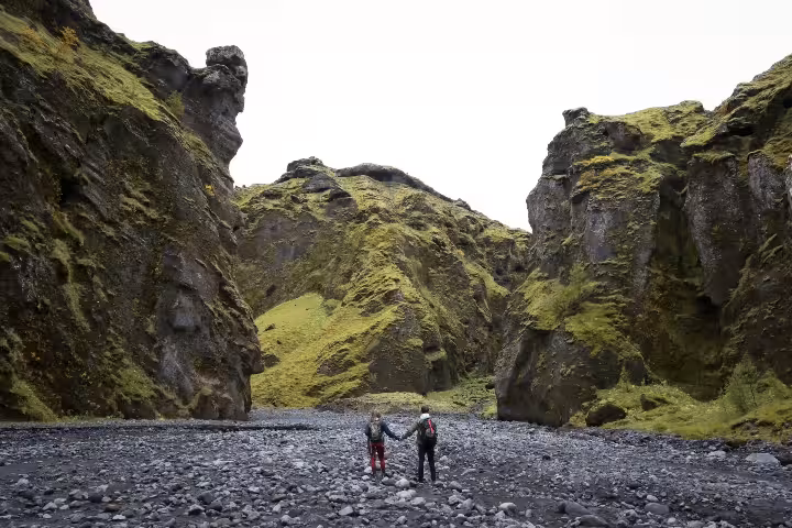 Couple holding hands while hiking through a vast mossy volcanic canyon on an express glacier and highland summer adventure tour.