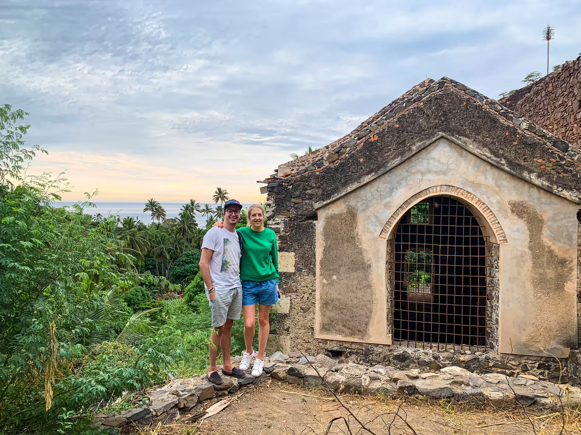 Couple standing by historic chapel in lush greenery during Cidade Velha tour with ocean view.
