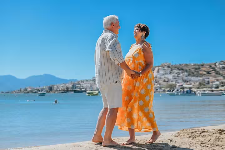 Couple holding hands and smiling at each other on a sandy beach in Elounda.