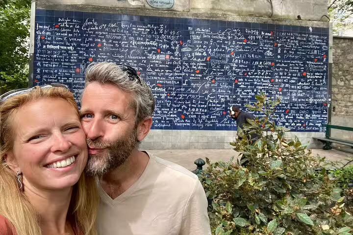 Couple smiling in front of the I Love You Wall in Montmartre, Paris