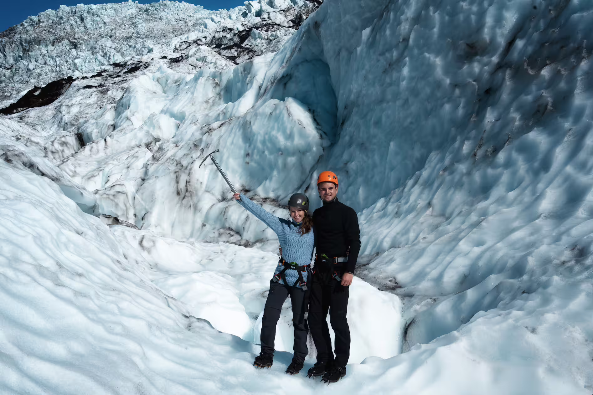 Happy couple in climbing gear holding an ice axe poses on Skaftafell glacier during an Iceland photoshoot adventure tour