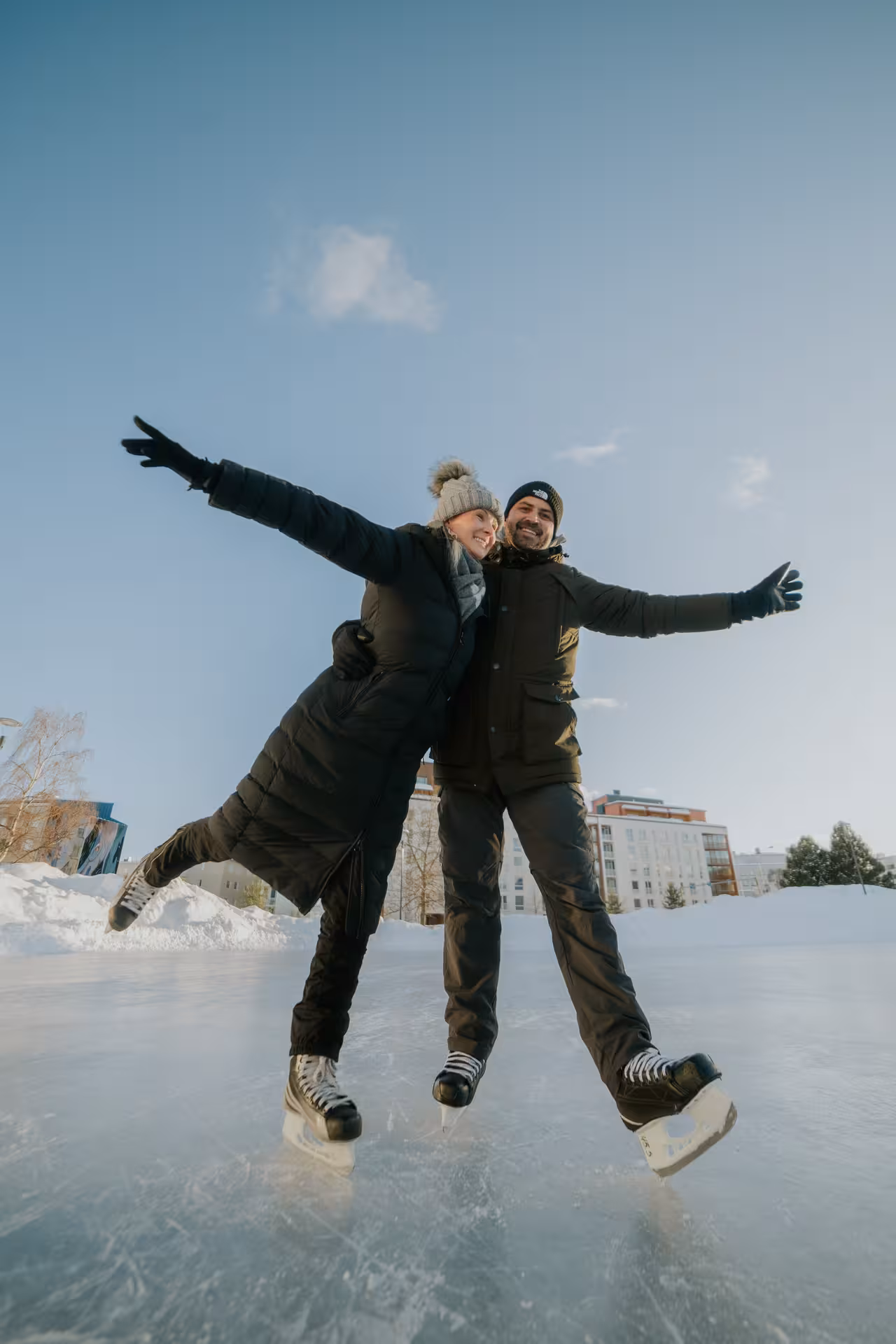 Happy couple posing with arms outstretched on an ice rink during a private photography session in Rovaniemi.