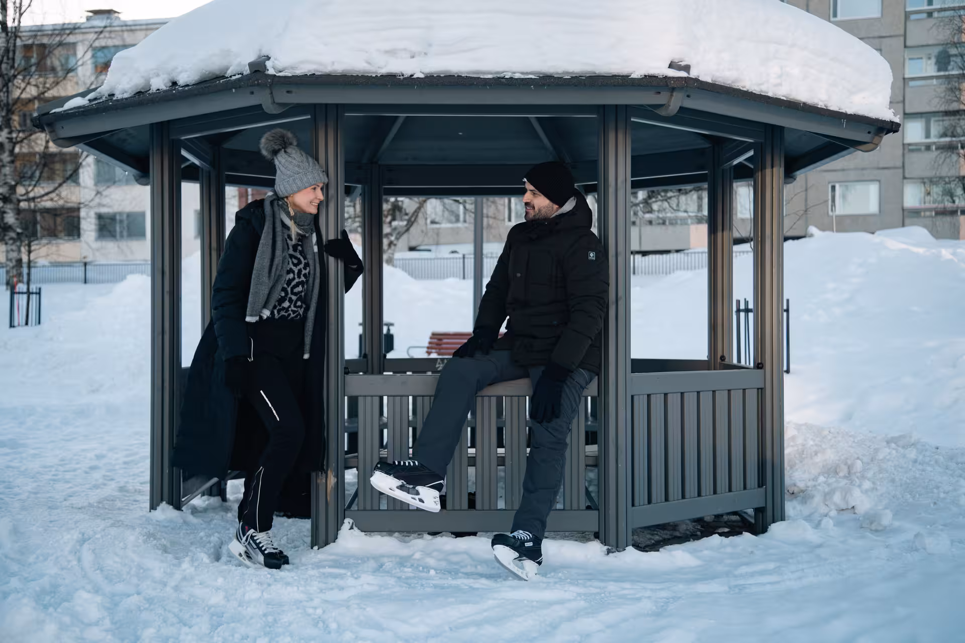 Couple enjoying a winter moment in Rovaniemi, sitting on a snowy gazebo during ice skating photography session.