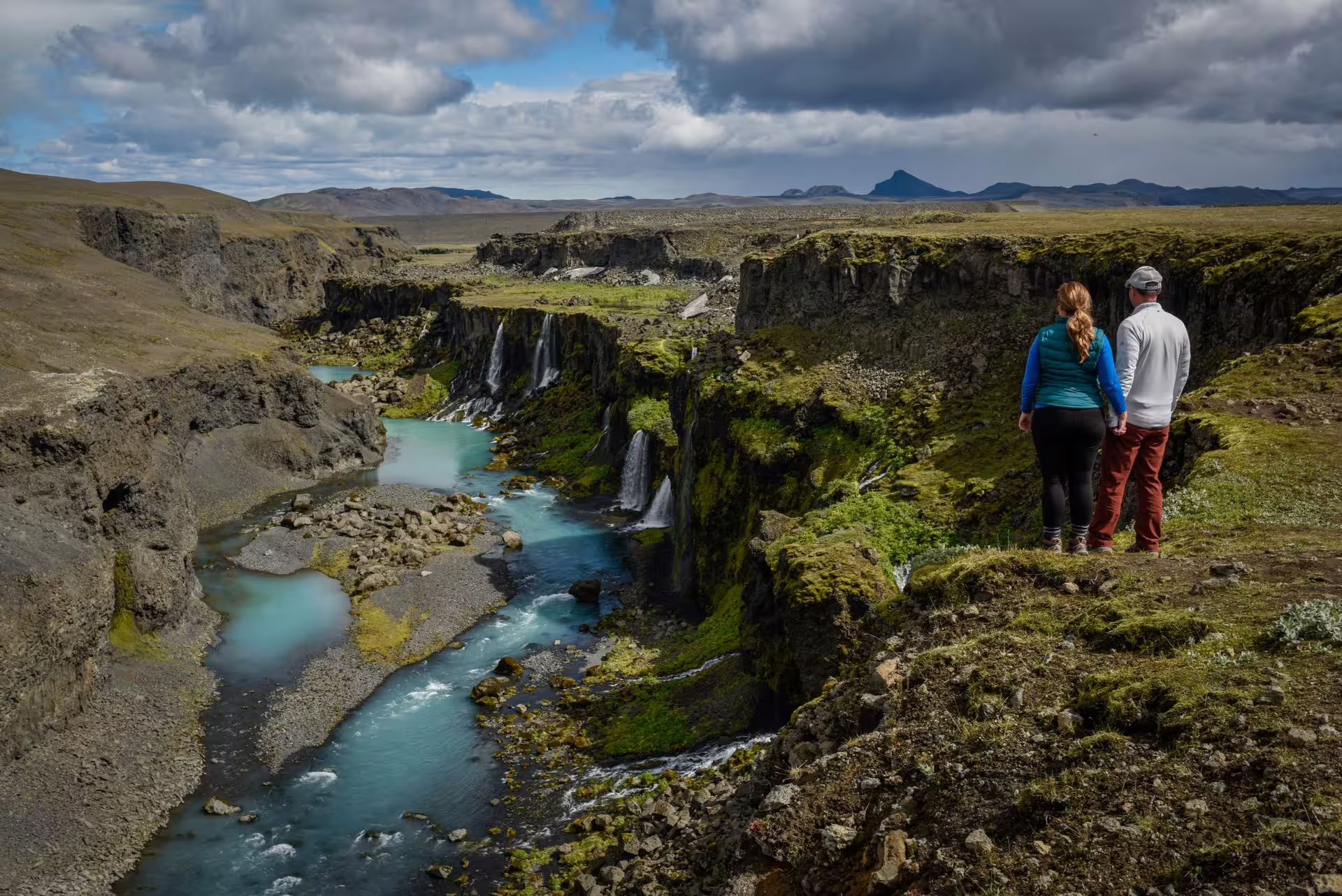 Couple admiring stunning Iceland canyon waterfall and turquoise river on a scenic 12-day grand tour