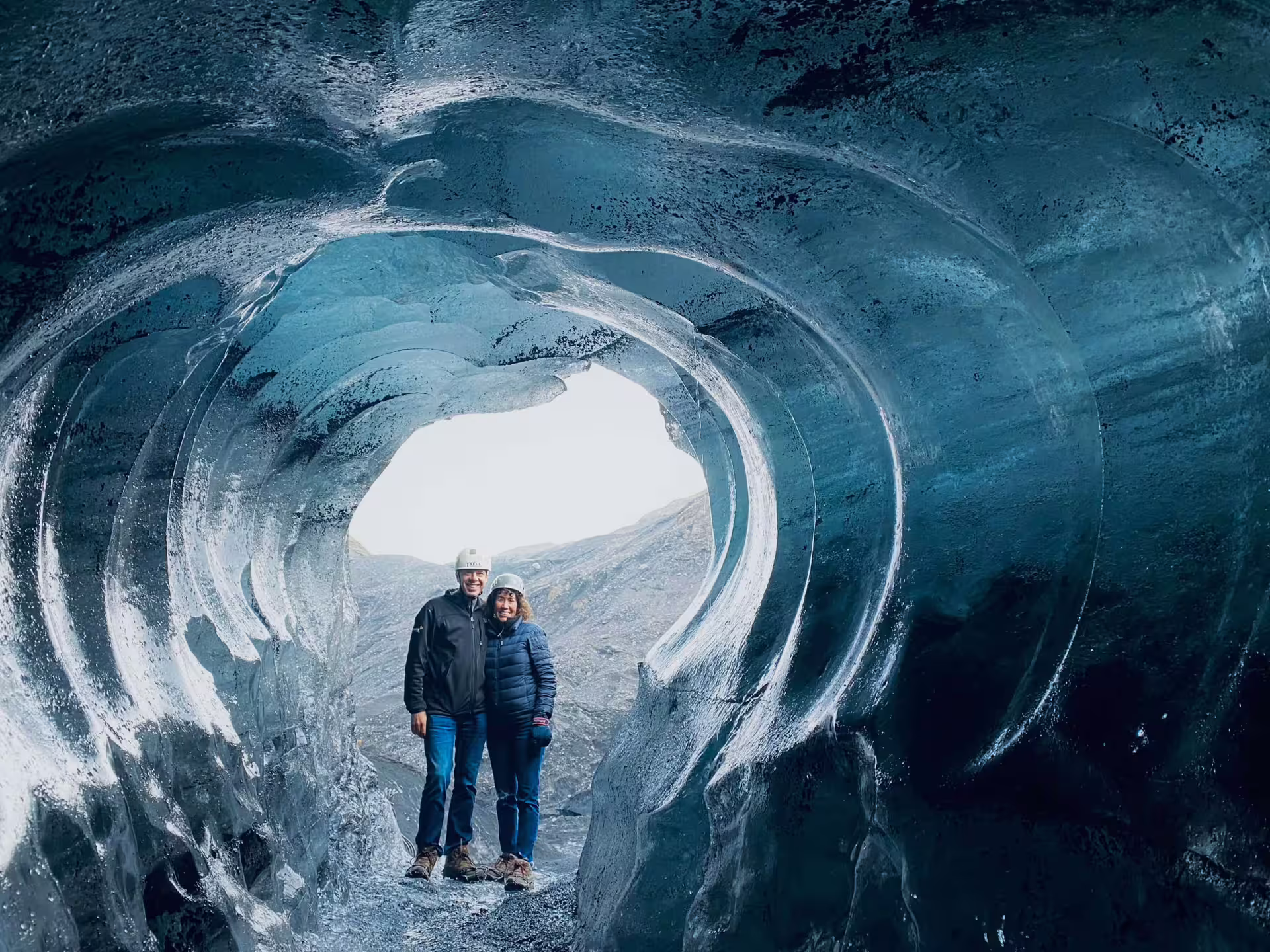 Couple in helmets standing inside a blue ice cave on Iceland's South Coast glacier tour