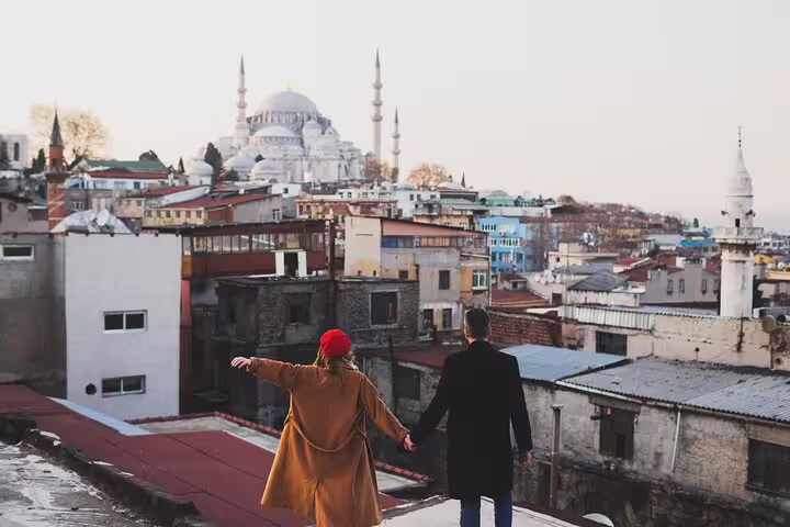Couple holding hands on Istanbul rooftop with Süleymaniye Mosque view, personal travel photographer tour