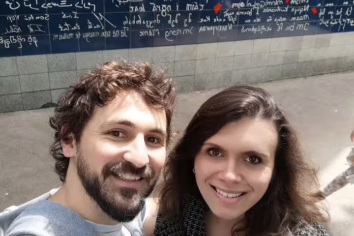 Couple smiling in selfie in front of the Je t'aime Wall in Montmartre, Paris