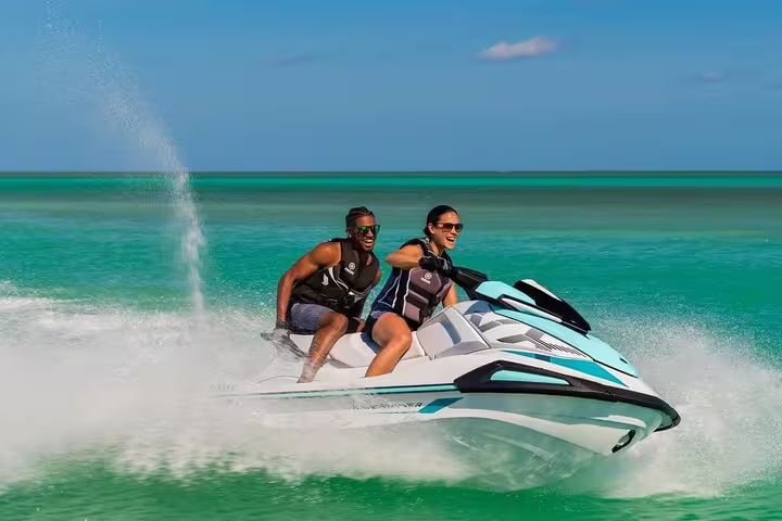 Couple riding a jet ski at speed on turquoise Ibiza sea, guided jet ski tour to Cala Comte adventure