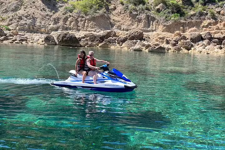 Couple riding a jet ski in crystal-clear Portitxol waters, guided excursion along Ibiza’s rocky coastline