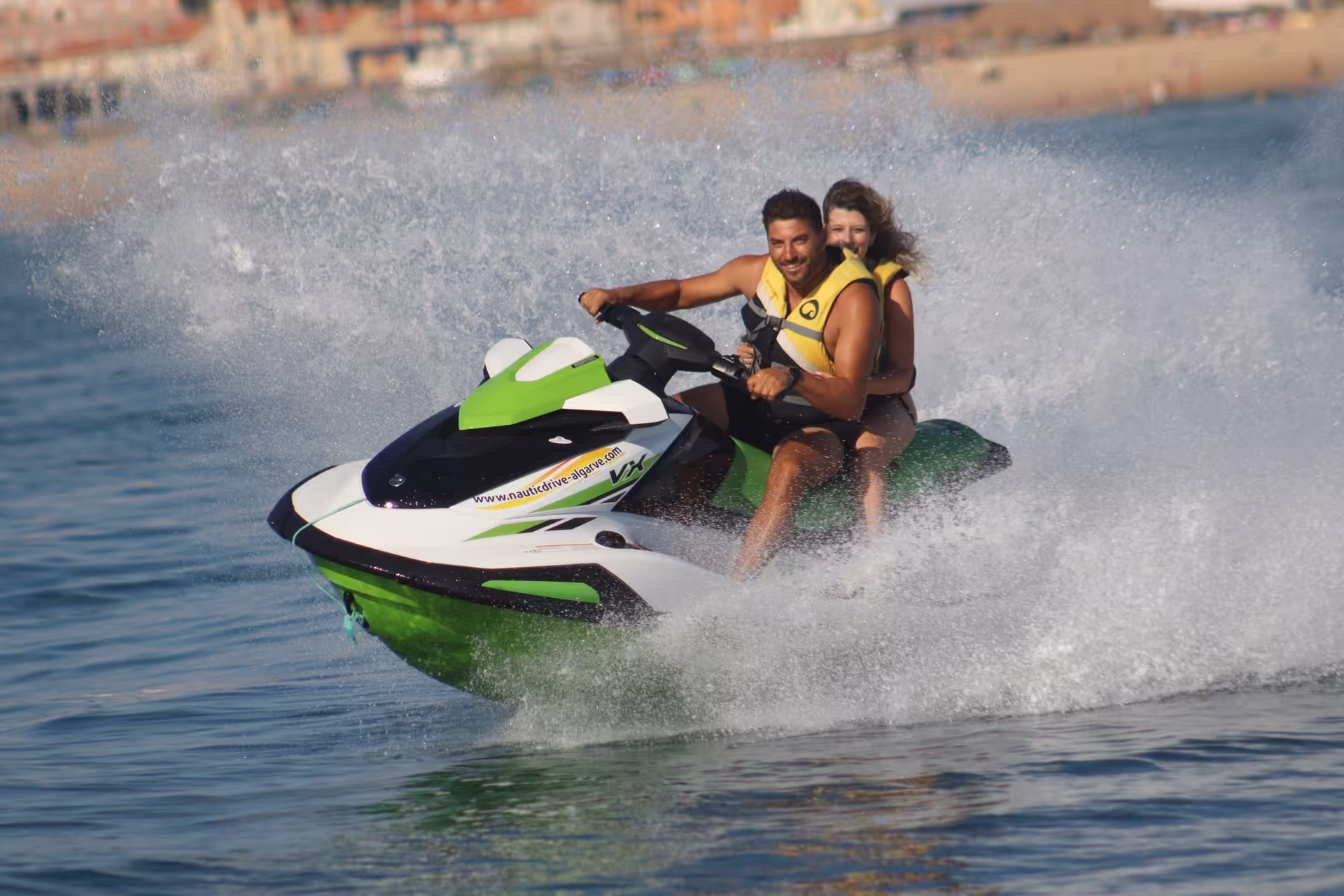 Couple riding a powerful jet ski through waves at Praia da Rocha Baixinha, Algarve coast jet ski rental experience