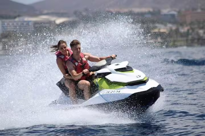 Excited couple enjoying an adventurous jet ski ride on sparkling ocean waters during a 1-hour safari tour.