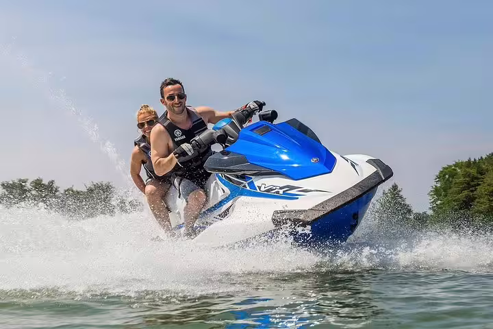 Couple riding a jet ski at speed near San Antonio Ibiza on the Es Vedrá excursion, splashing through waves