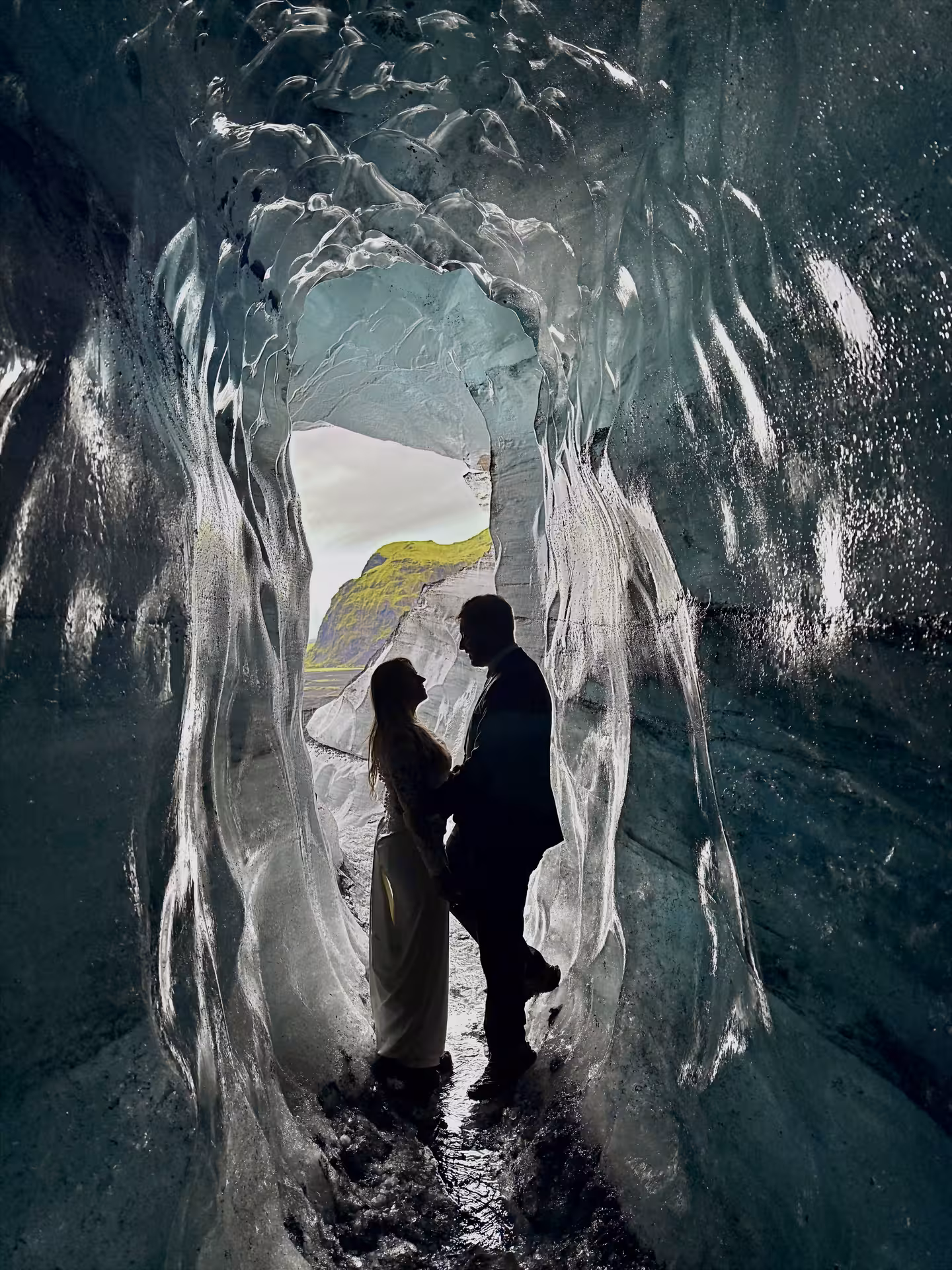Couple silhouetted inside Katla ice cave on a private tour, crystal walls and view toward Vík, Iceland