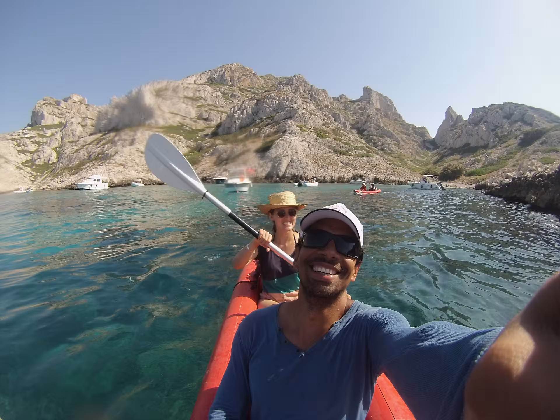 Couple kayaking in the Calanques of Marseille on clear turquoise water with limestone cliffs and boats nearby