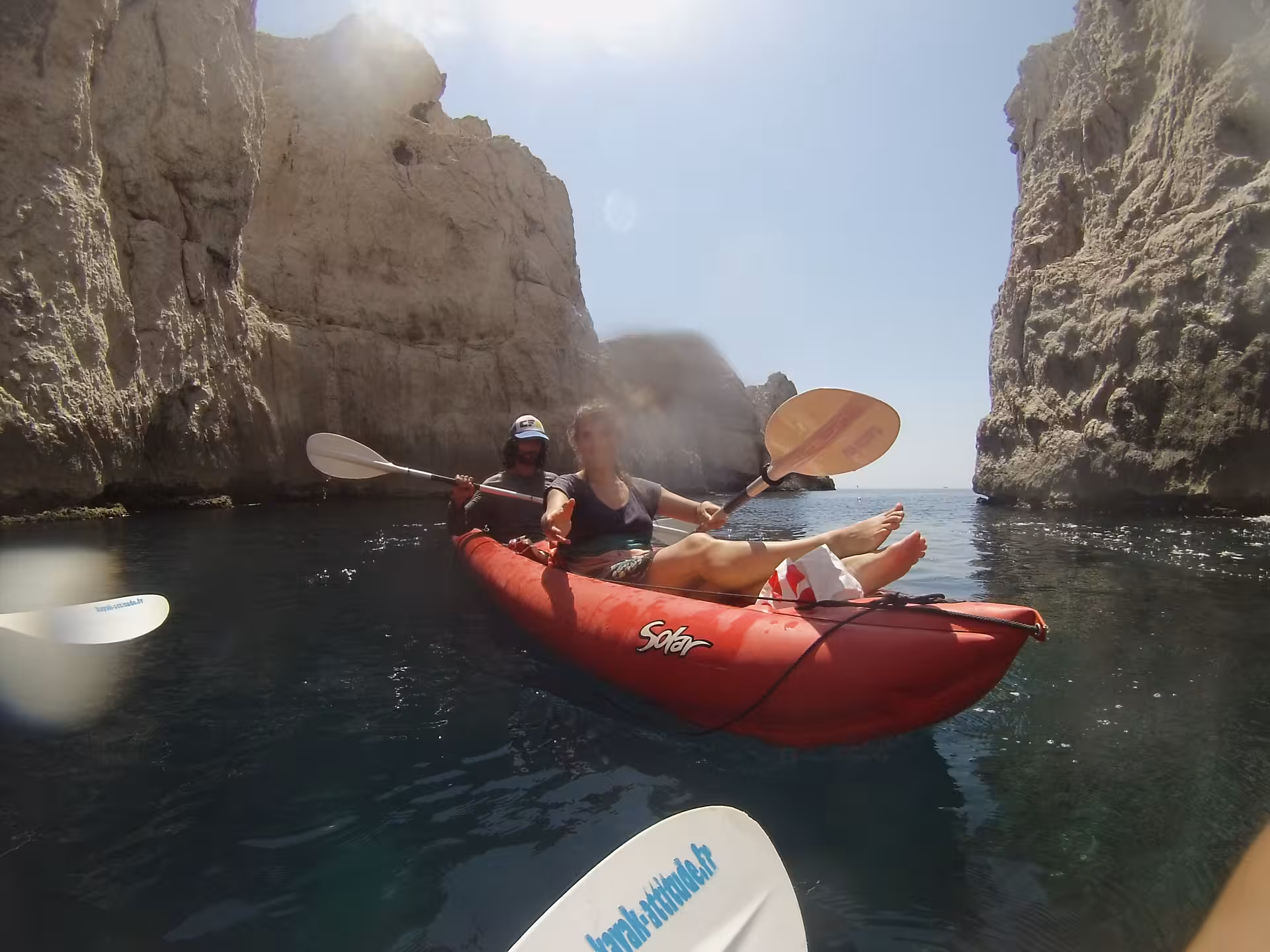 Couple kayaking through a narrow Calanques inlet near Marseille, calm turquoise water and towering cliffs