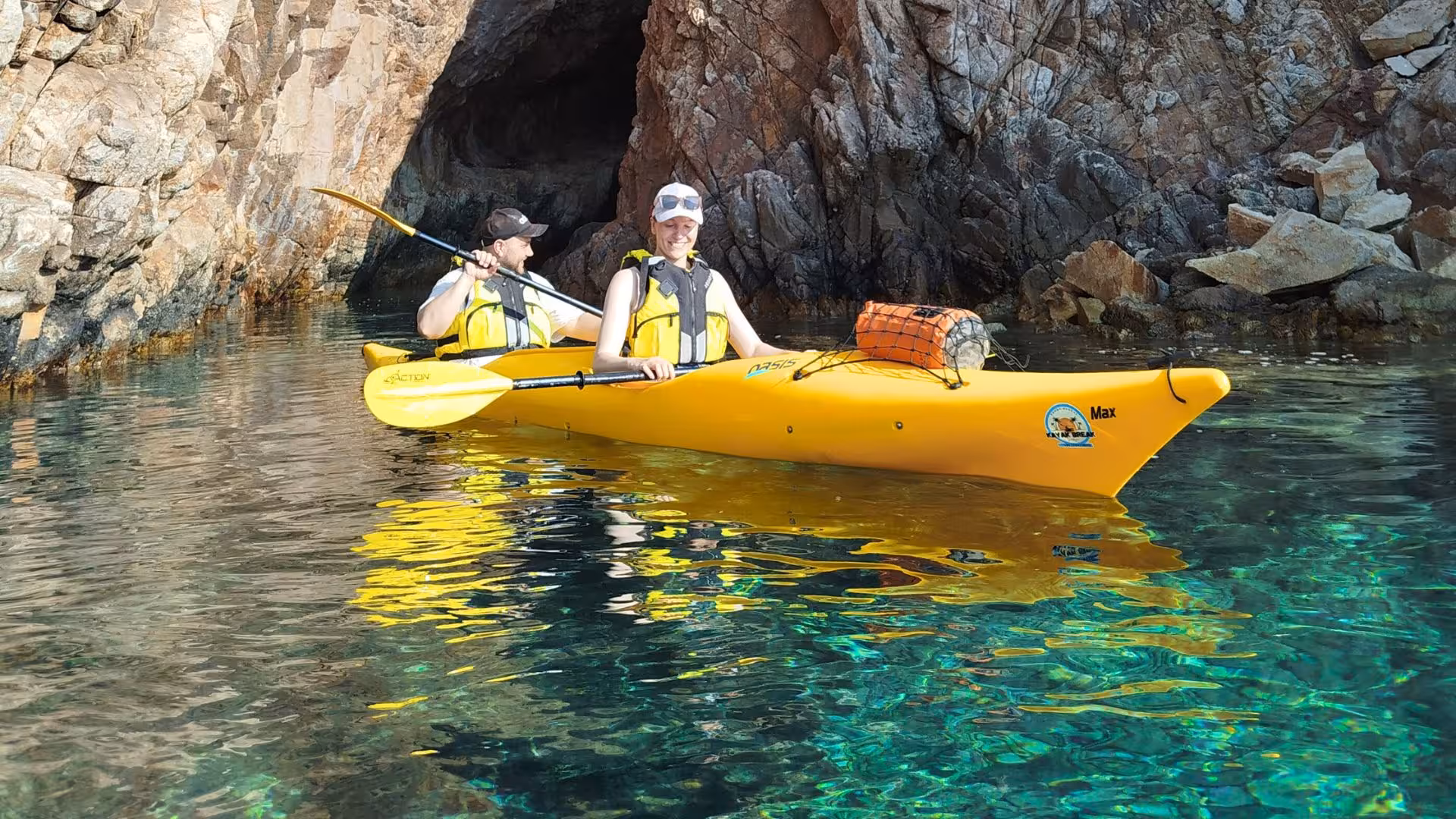 Couple kayaking through crystal-clear waters near rocky cliffs on Tuerredda tour in Chia.