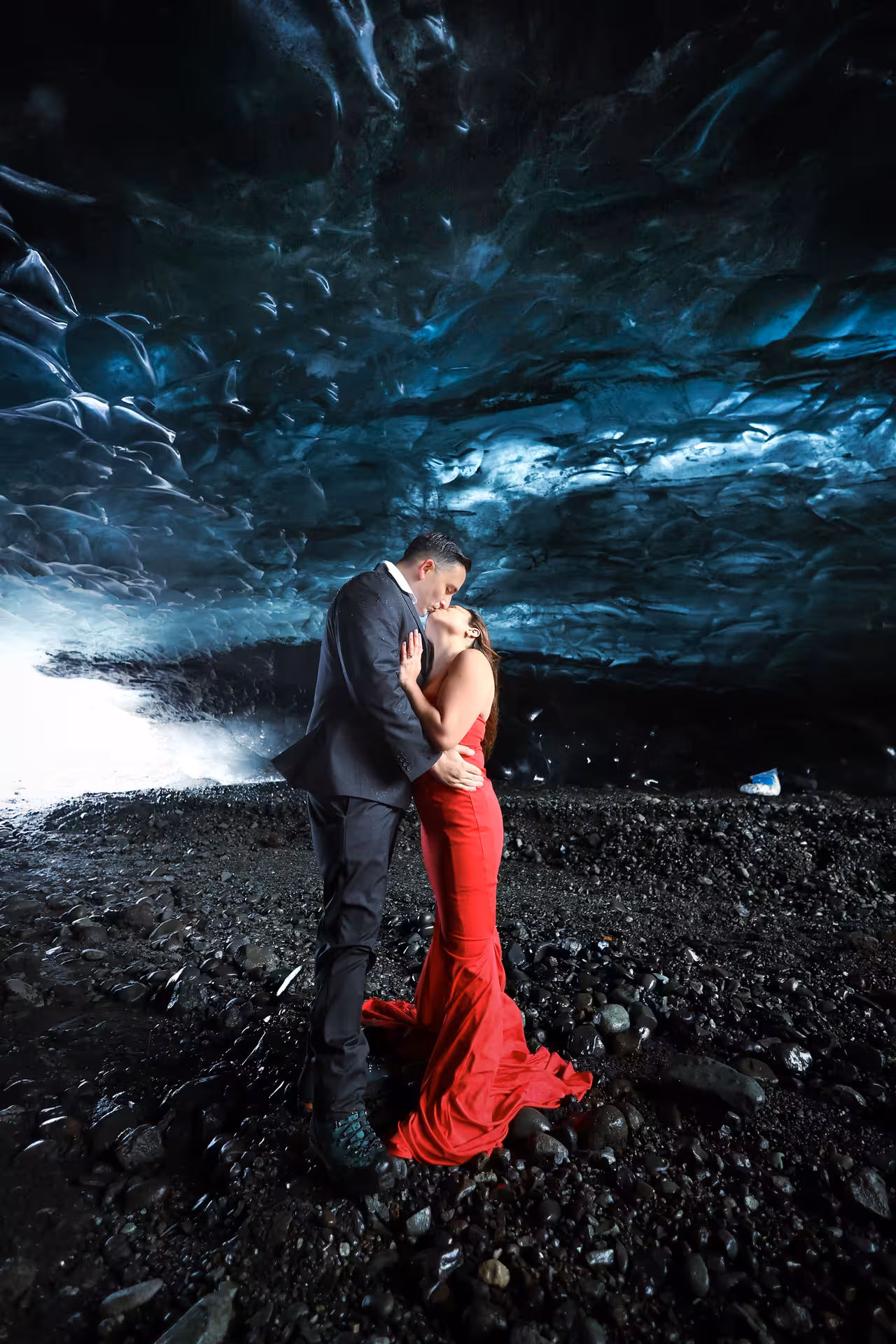 Romantic couple sharing a kiss inside a glowing blue ice cave during an Iceland glacier lagoon proposal tour experience.