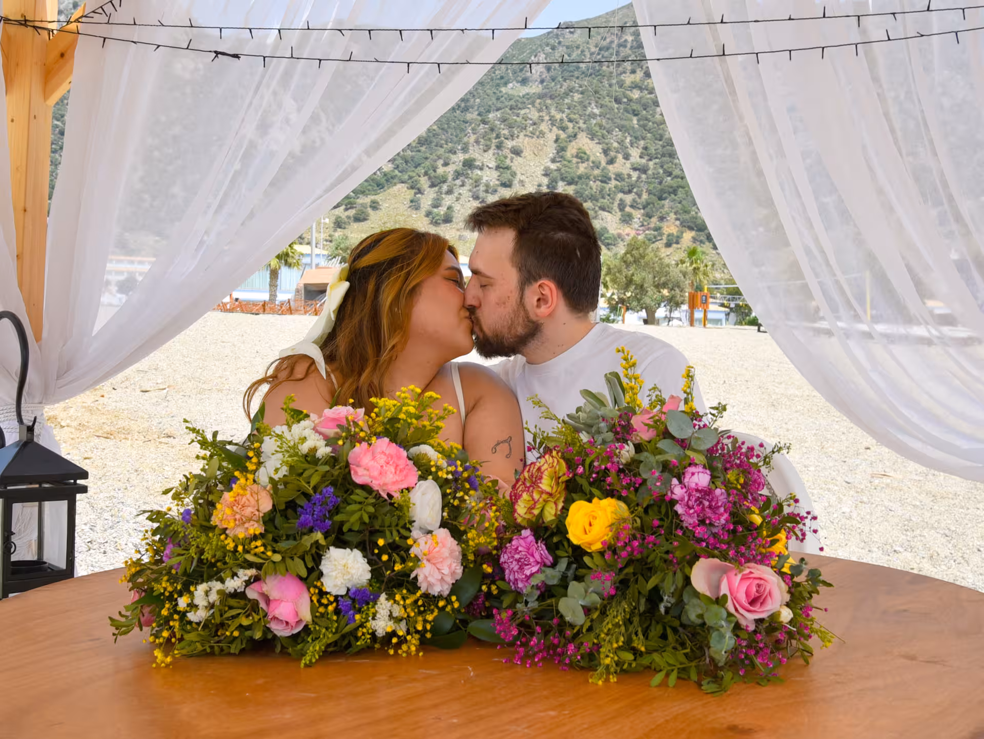 Couple kissing behind vibrant floral arrangements under a canopy at Heraklion Venetian Port, ideal for anniversary celebrations.