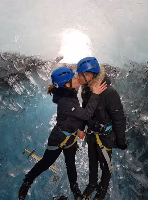 Couple kissing inside Vatnajokull glacier ice cave wearing blue helmets and harnesses