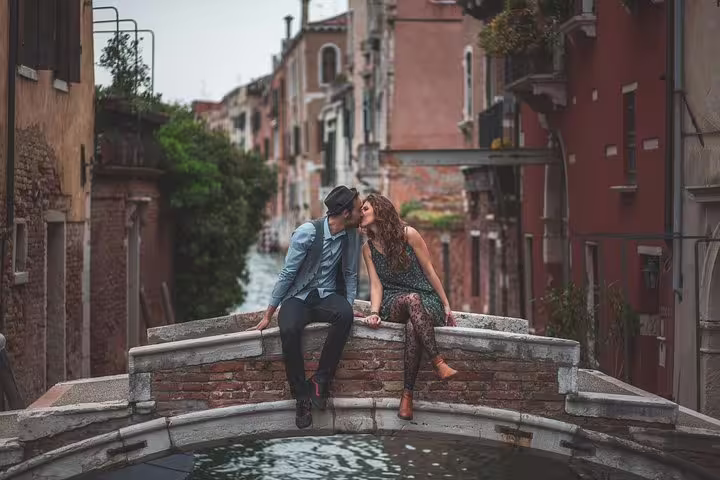 Couple kissing on a Venice canal bridge during a romantic city portrait session with charming streets behind