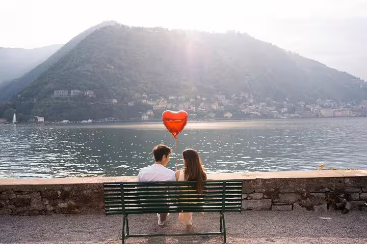 Romantic couple on bench with heart balloon by Lake Como, private travel photographer tour at golden hour