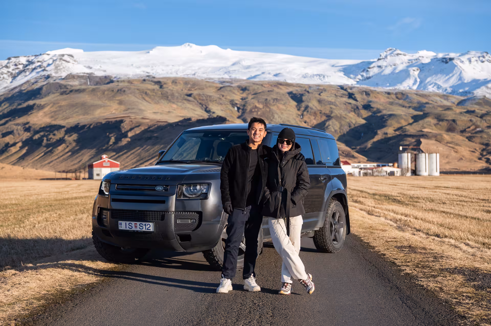 Couple posing in front of a Land Rover Defender on Iceland's South Coast with snow-capped mountains behind