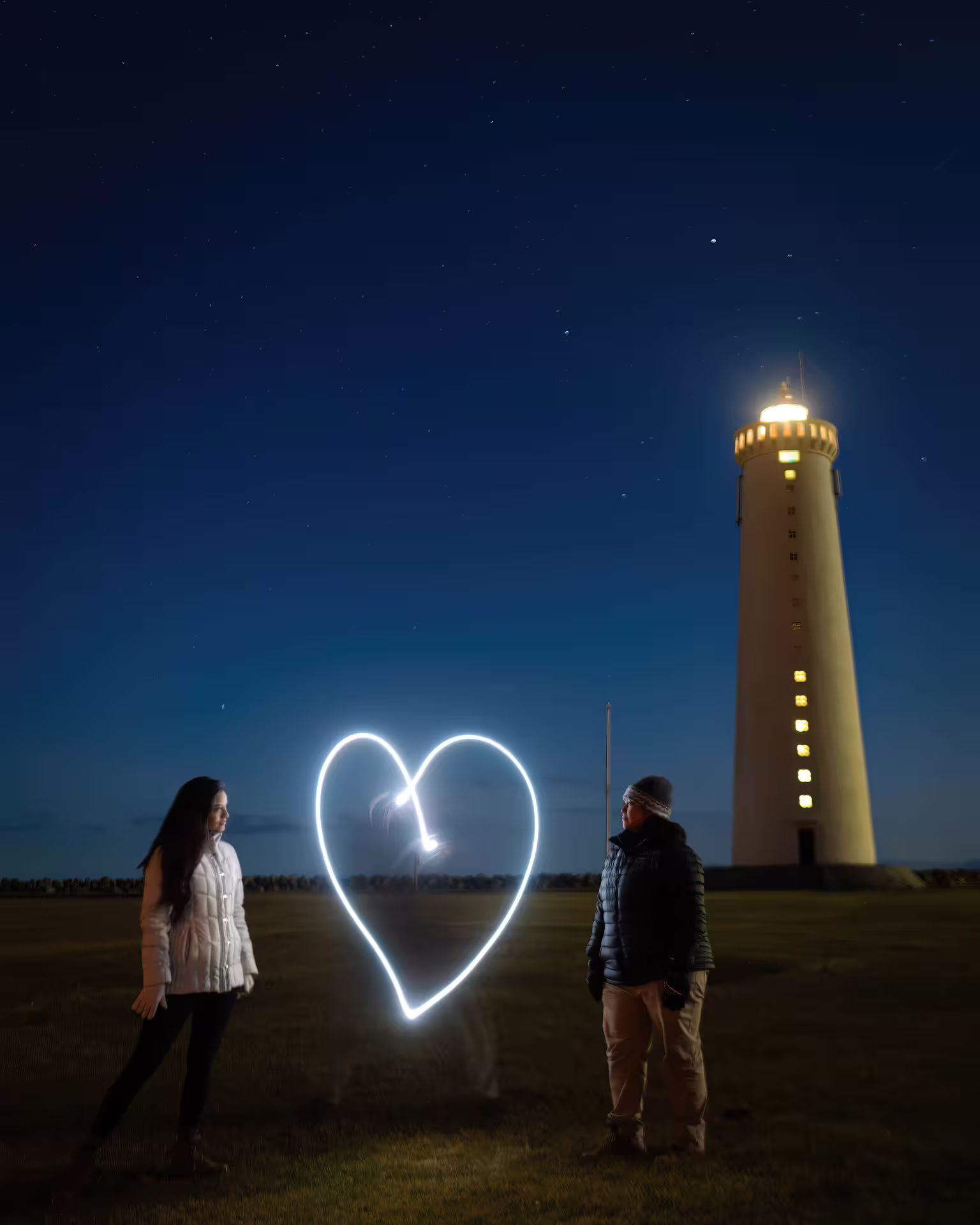 A couple poses with a light-painted heart near an Iceland lighthouse on a creative private northern lights photography tour