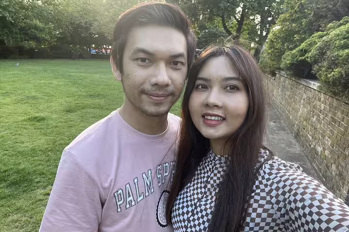 Couple smiling outdoors in a London park near a brick wall during a walking tour
