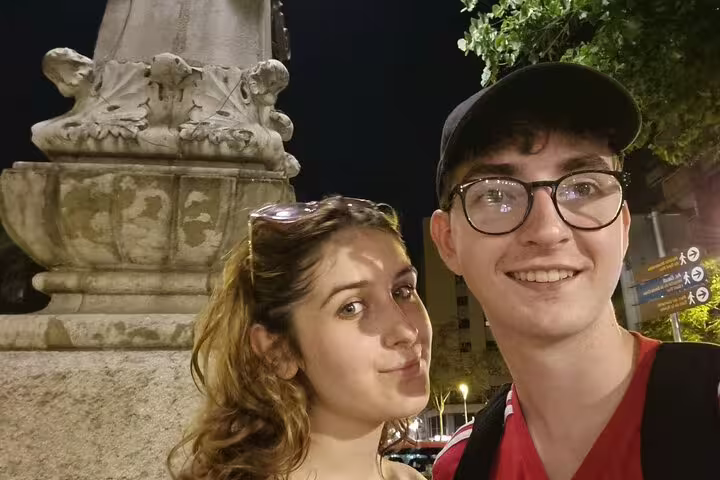Couple smiling at night near ornate stone monument base in Barcelona city center