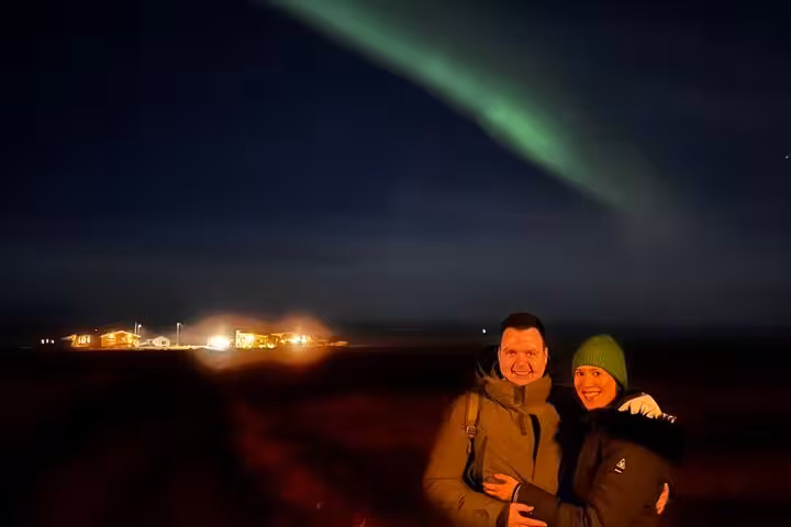 Couple smiling under green northern lights aurora borealis at night near Reykjavik Iceland