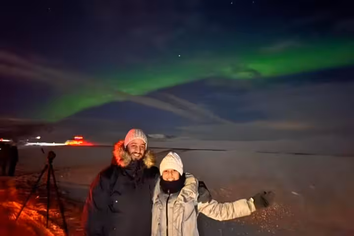 Couple posing under vibrant green northern lights aurora borealis on snowy Reykjavik landscape at night