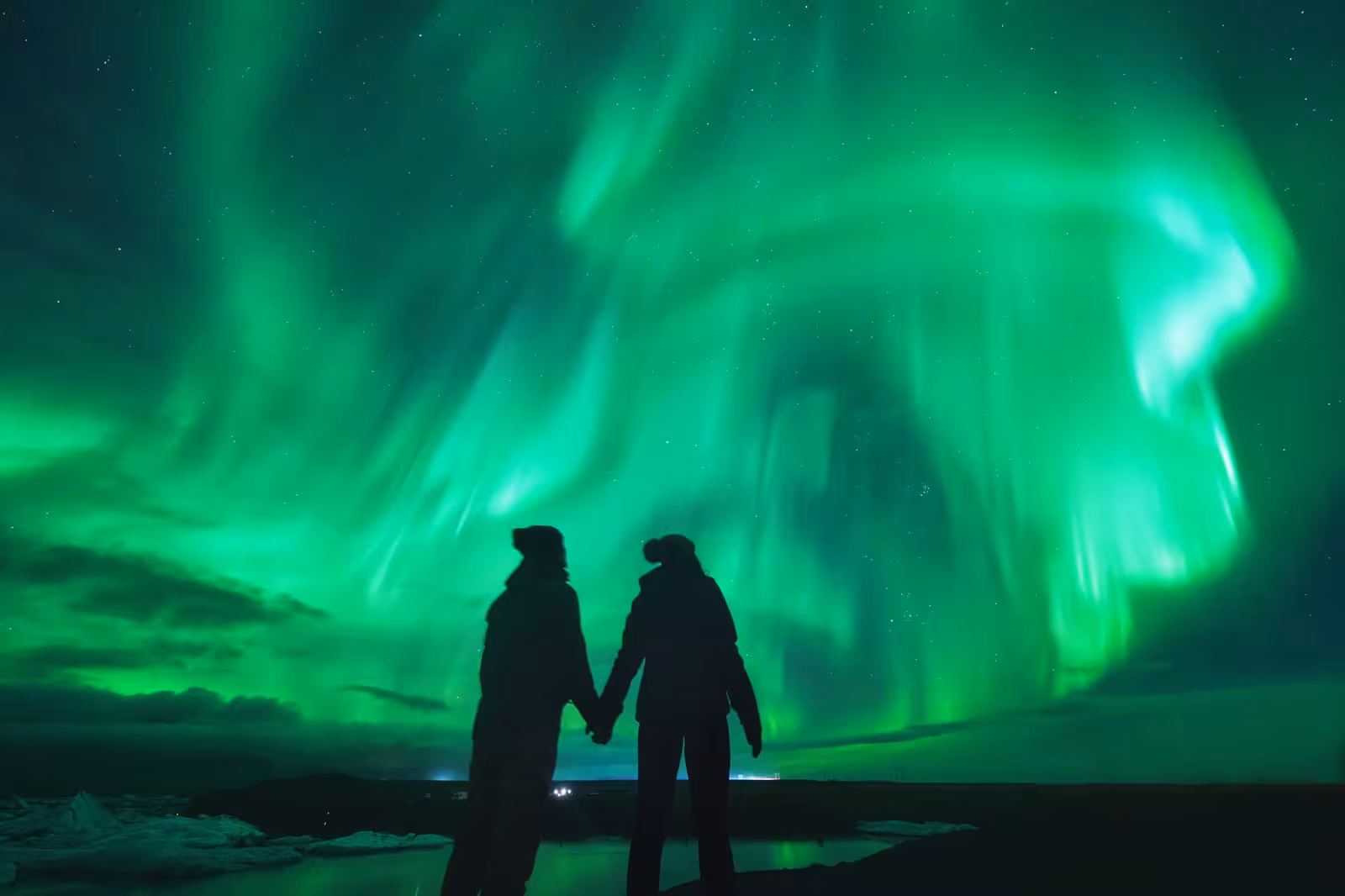 Couple holding hands under vibrant Northern Lights on a 5-Day Icelandic Glacier Lagoon Tour.