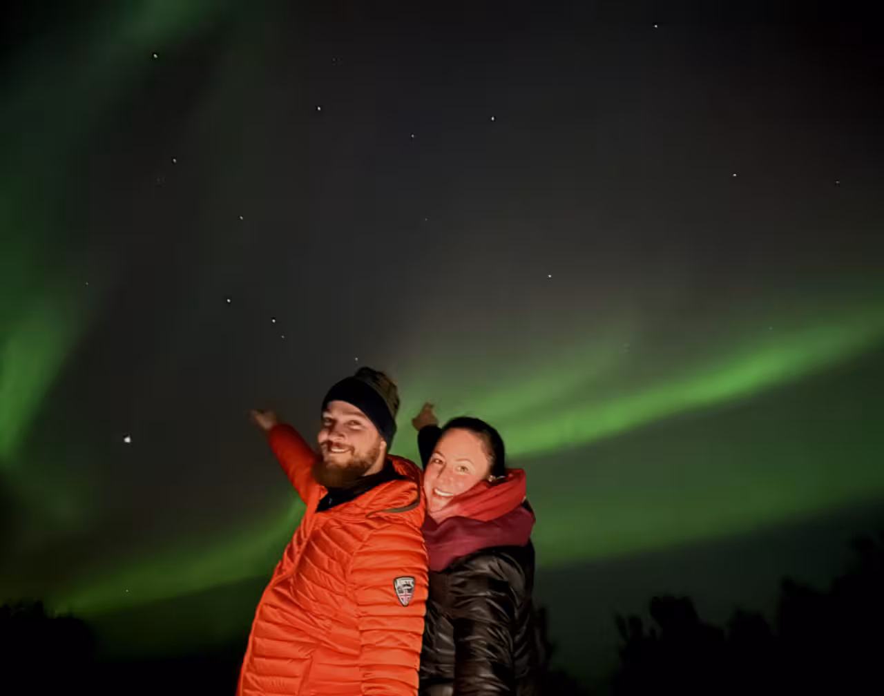 Couple smiling under vivid green northern lights in Iceland night sky