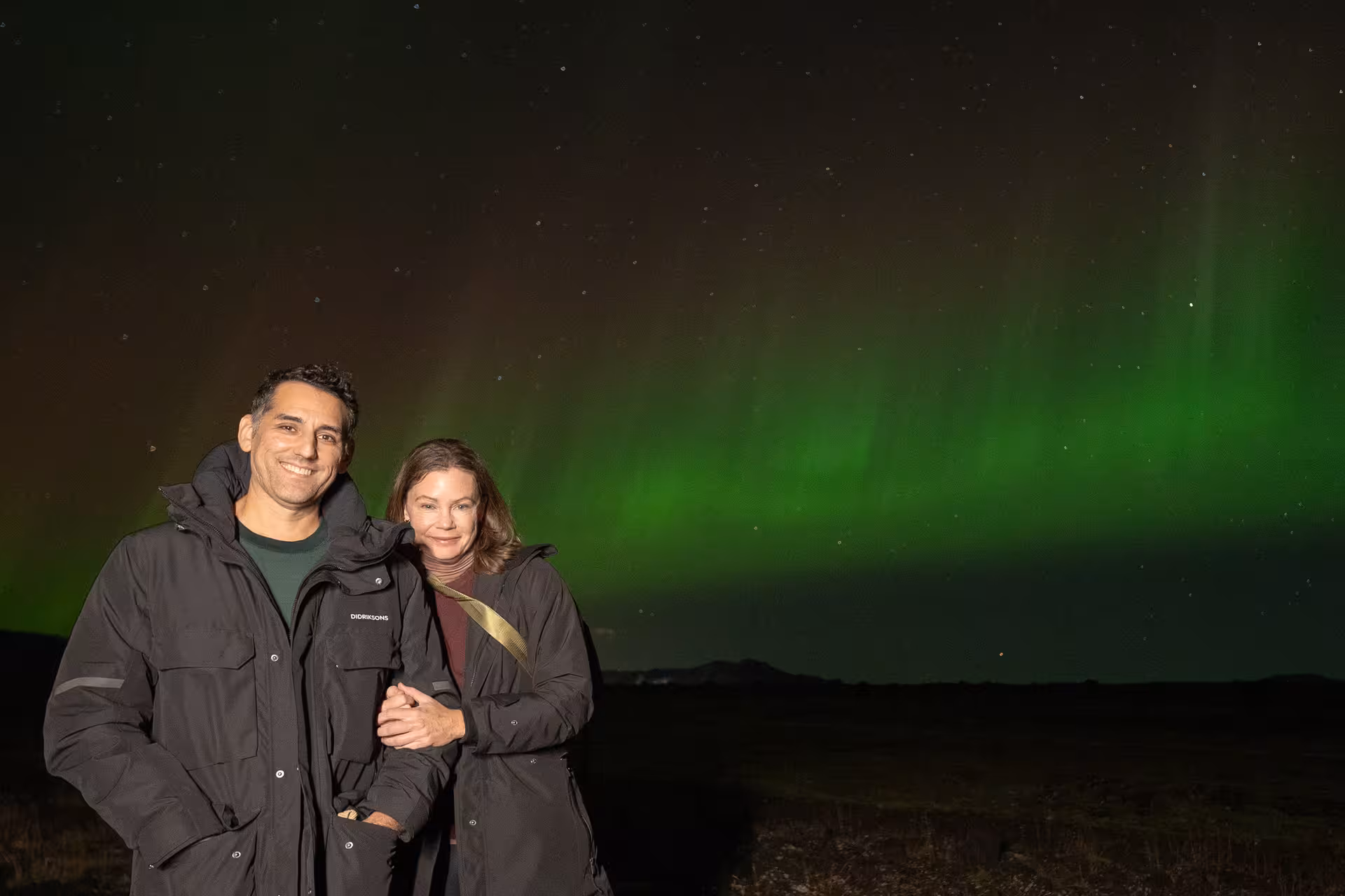 Couple smiling under vibrant green northern lights aurora borealis in Iceland night sky