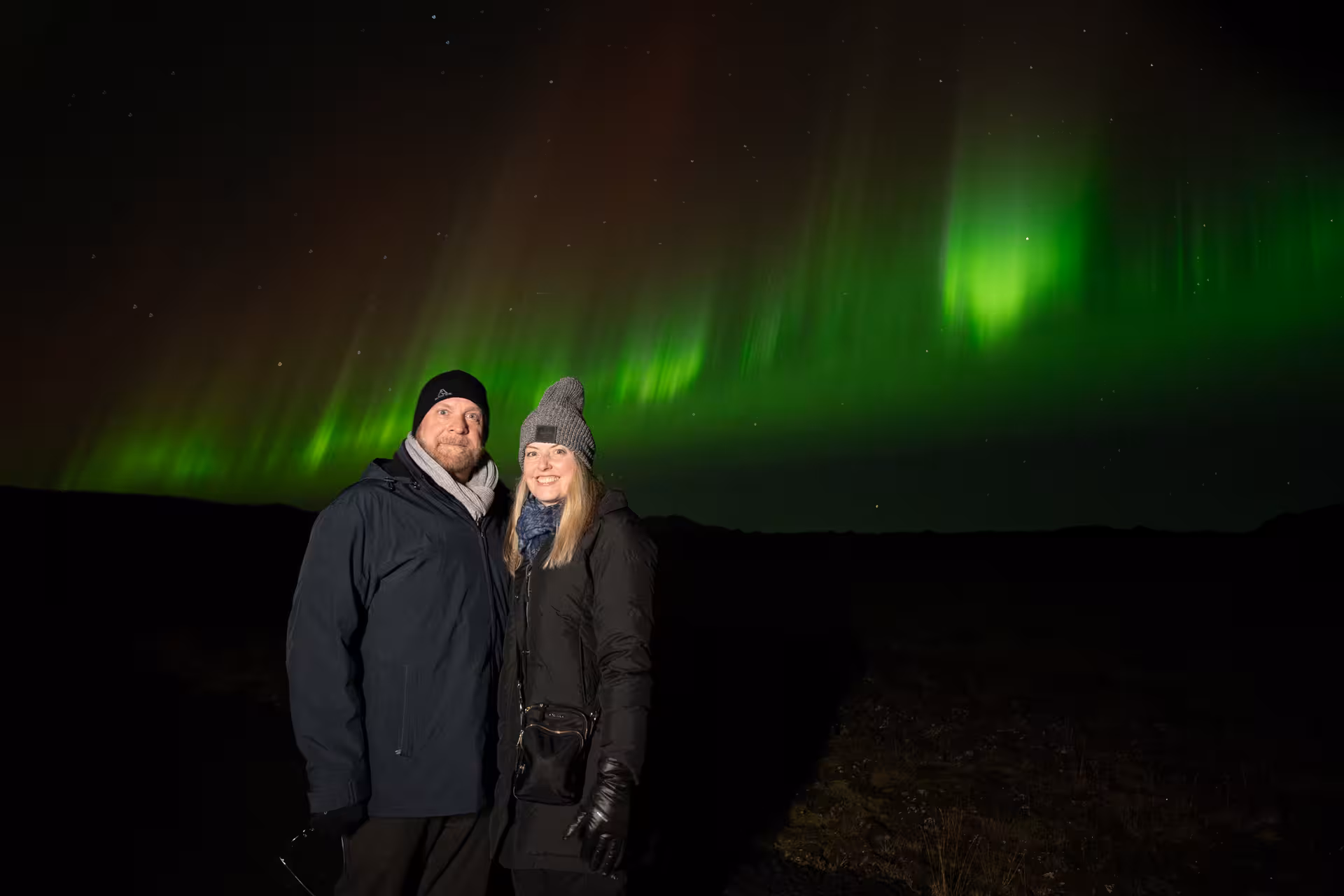 Couple smiling under vibrant green and red northern lights in Iceland night sky