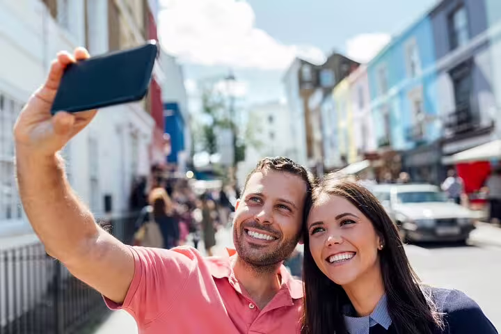 A couple takes a selfie with colorful houses in the background during a private Notting Hill tour in London, capturing vibrant market life.