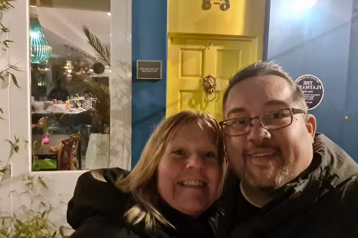 Couple smiling outside a yellow door and restaurant window in Notting Hill at night