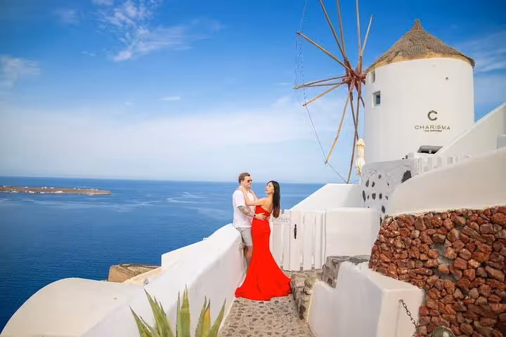 Couple by Oia windmill overlooking the Aegean, Santorini day getaway with luxury villa stay and transfers