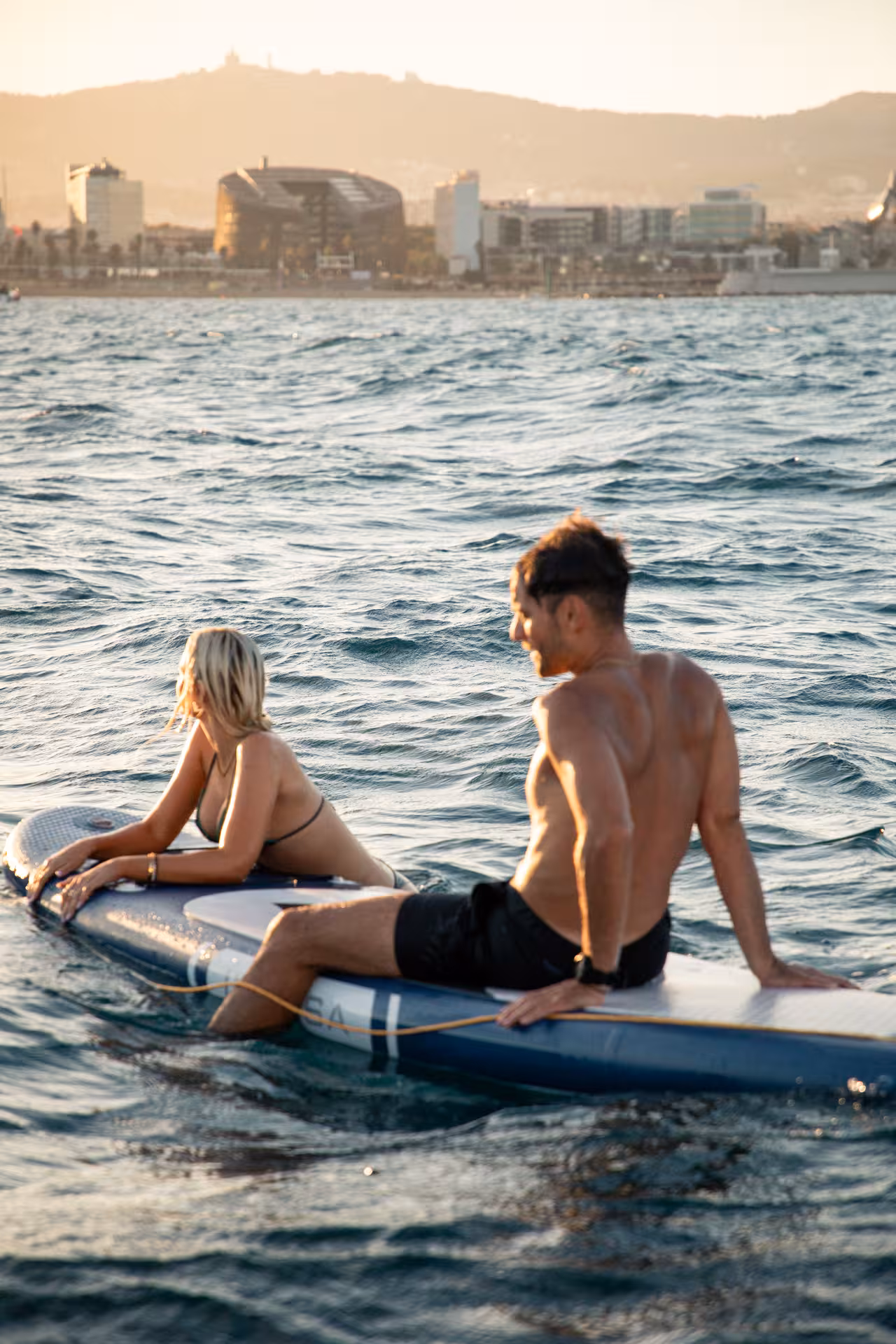 Couple on paddleboard at sunset off Barcelona during 4-hour private luxury Bali 4.2 catamaran cruise