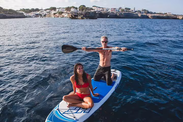 Couple enjoying stand-up paddleboarding on crystal-clear waters during a private catamaran tour in Ibiza and Formentera.