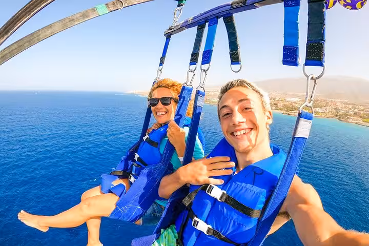 Smiling couple parasailing over the Red Sea in Sharm El Sheikh, with private transfer included in tour