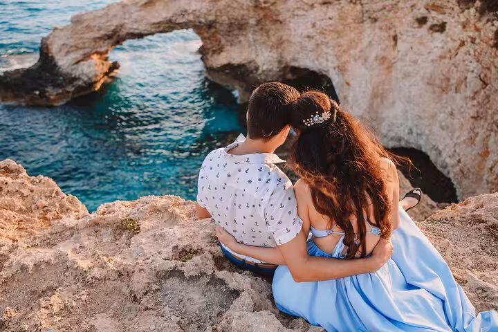 Couple embraces on a rocky Ayia Napa cliff overlooking turquoise waters, captured during a professional photoshoot.