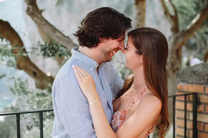 Smiling couple embraces under lush trees in Naples, capturing a candid moment during a private photoshoot.