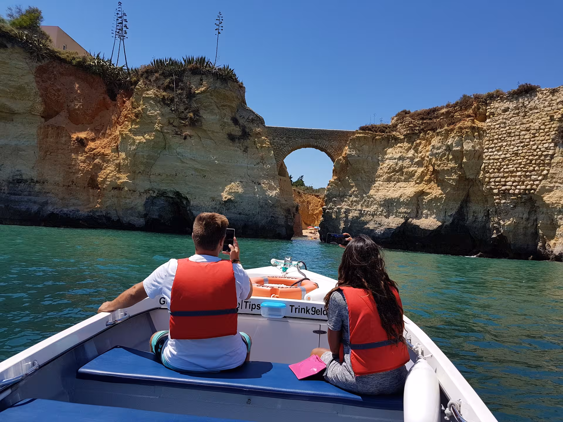 Couple on Algarve boat trip approaching stone arch and golden cliffs near Ponta da Piedade caves in sunny Lagos, Portugal