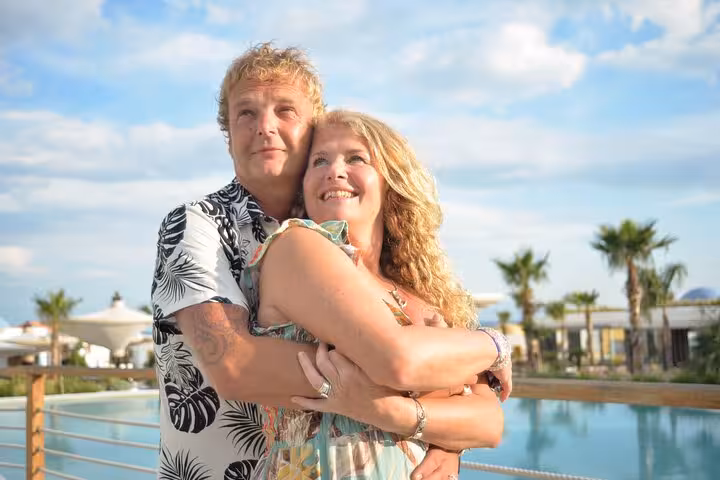 Happy couple embracing by a luxurious poolside with palm trees in the background during a Malia photoshoot session.