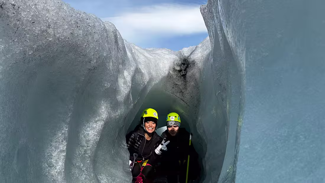 Two people posing for a photo inside a mini crevasse of ice on a glacier 