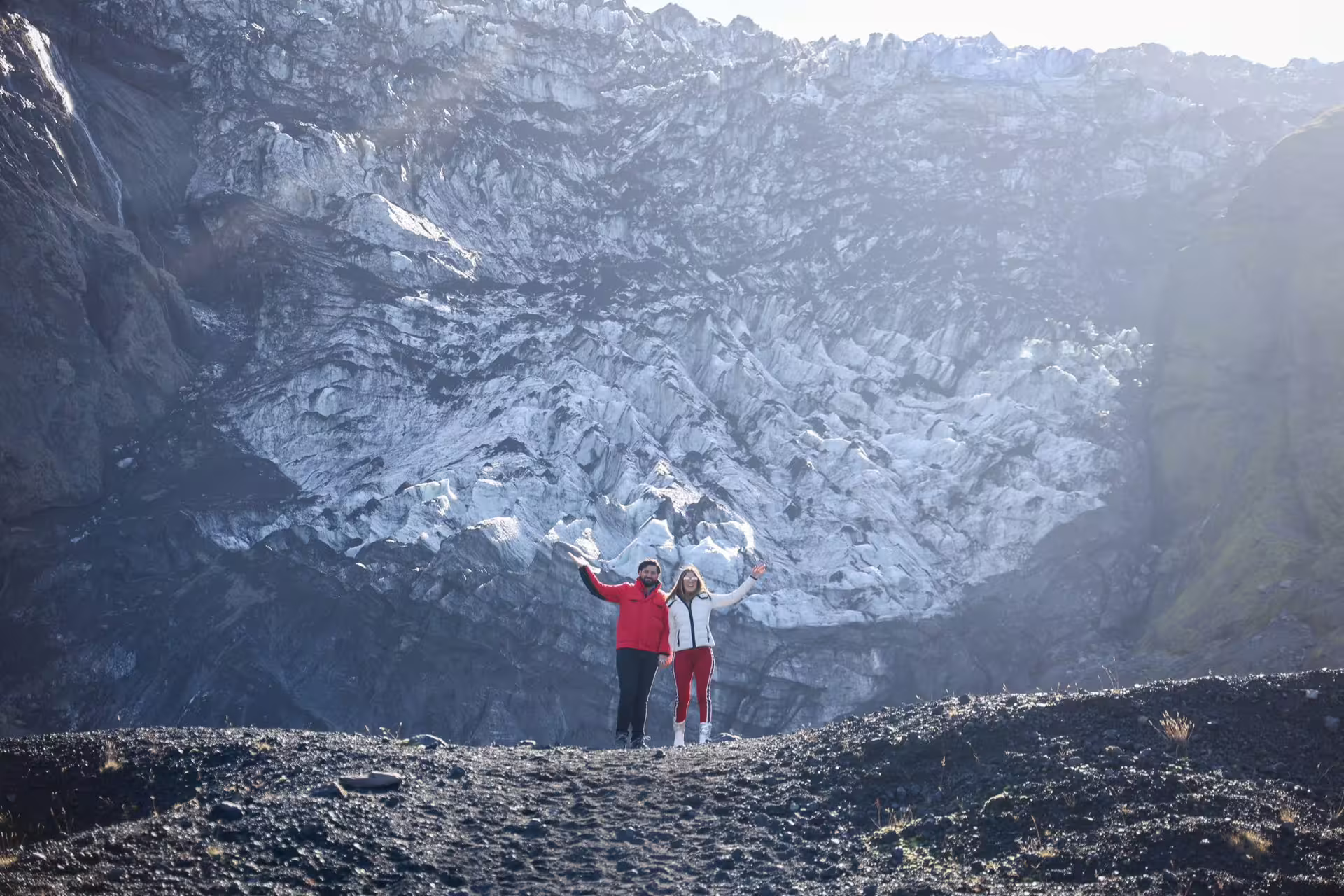 Couple posing joyfully in front of a massive Iceland glacier on a 12-day Grand Tour adventure