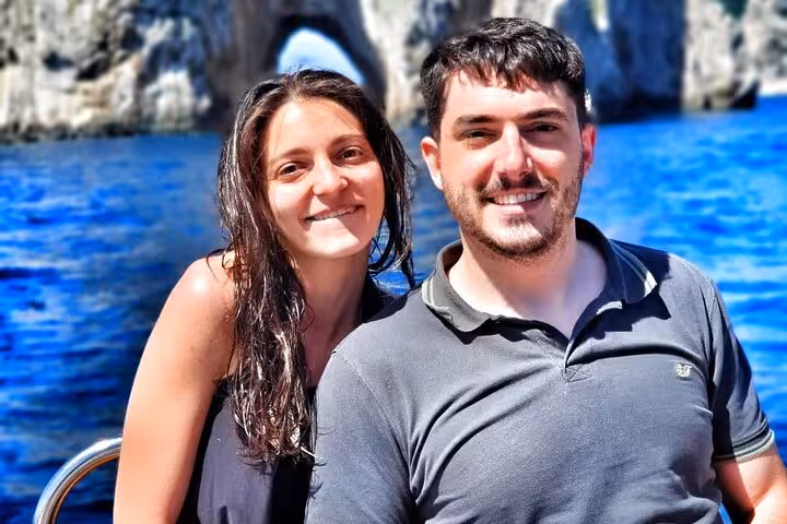 Couple enjoying a sunny day on a private boat tour near the iconic Faraglioni rocks in Capri.